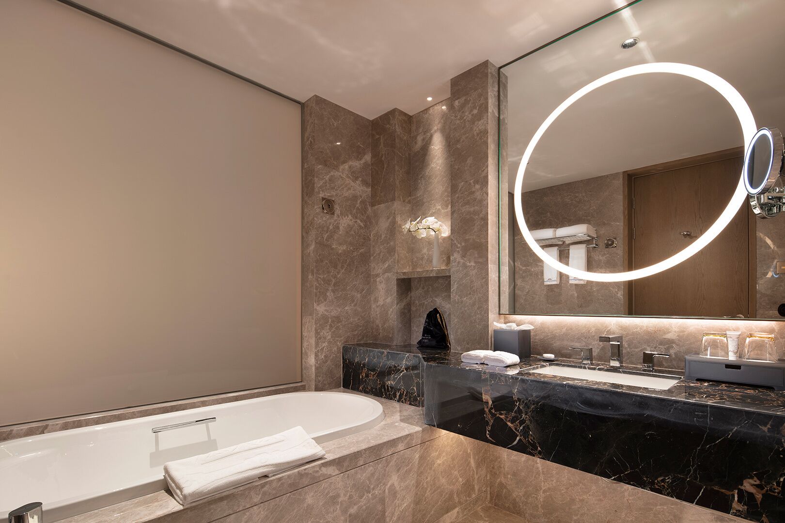 A modern bathroom with a bathtub, a vanity with a large mirror, and marble countertops.