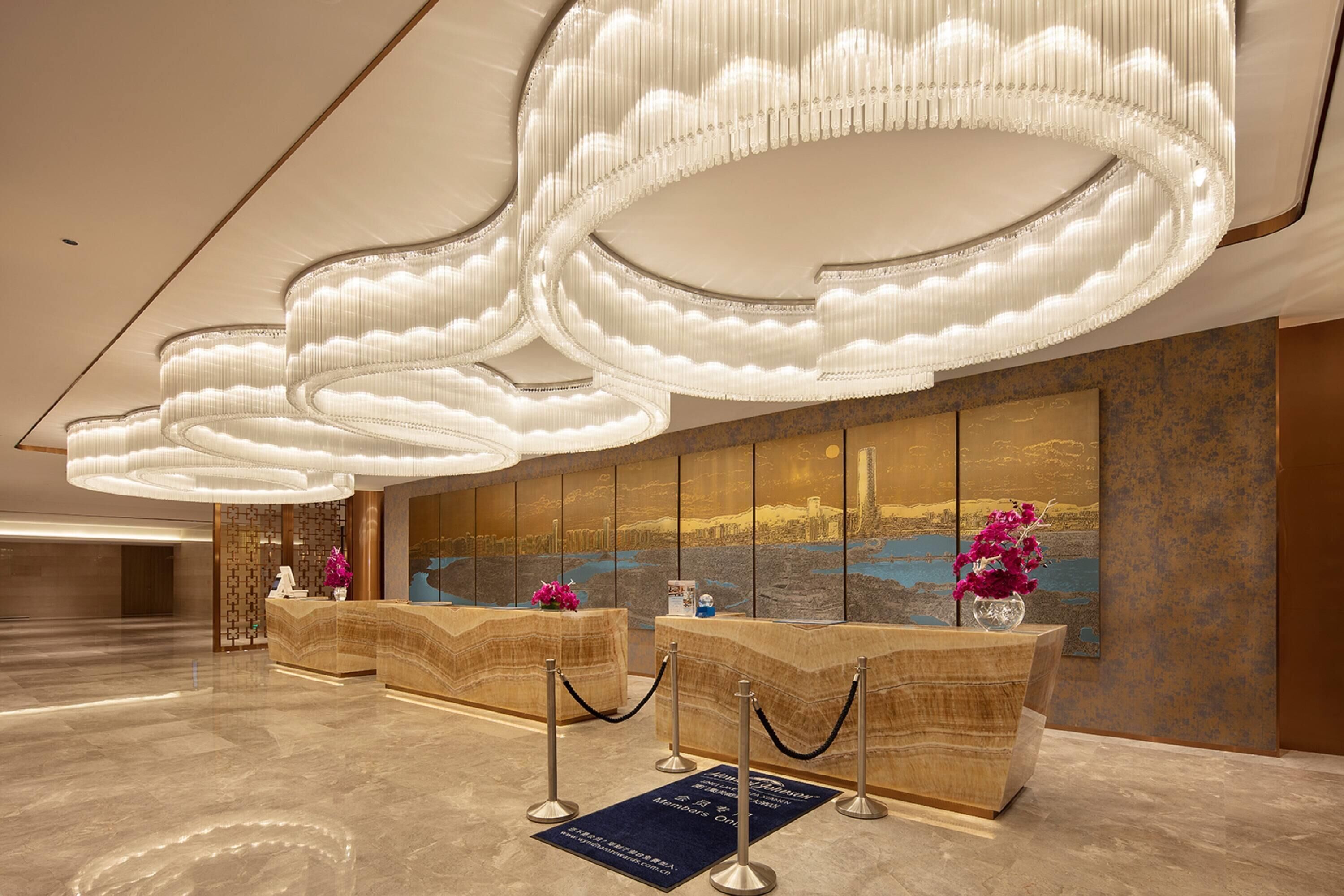 A lobby with a reception desk, a large wall mural, and a modern chandelier.