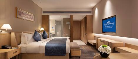 A modern hotel room with a large bed, bedside tables, a desk, and a TV.
