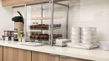 Une vitrine de pâtisserie remplie de viennoiseries, un coin café et des gobelets jetables.