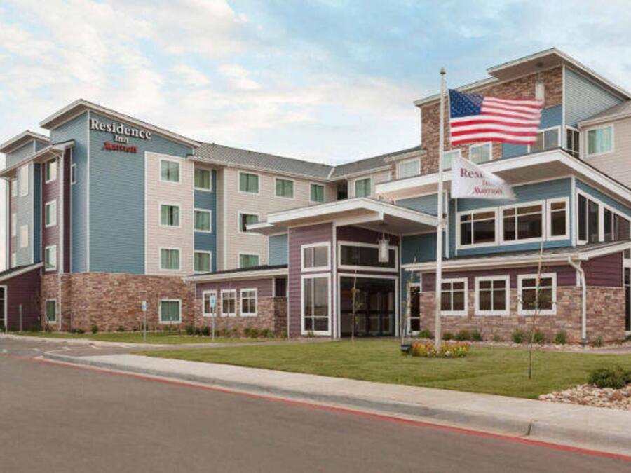 Um hotel com vários andares, exibindo uma bandeira americana destacada, uma entrada coberta e uma placa com a inscrição "Residence Inn".