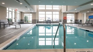 A large indoor swimming pool with clear glass walls, a lifebuoy, and a poolside area with chairs and tables. - Residence Inn by Marriott Toledo West (Toledo)