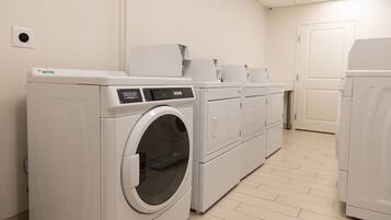 A laundry room with a front-loading washer and dryer, a white tiled floor, and a door in the background.