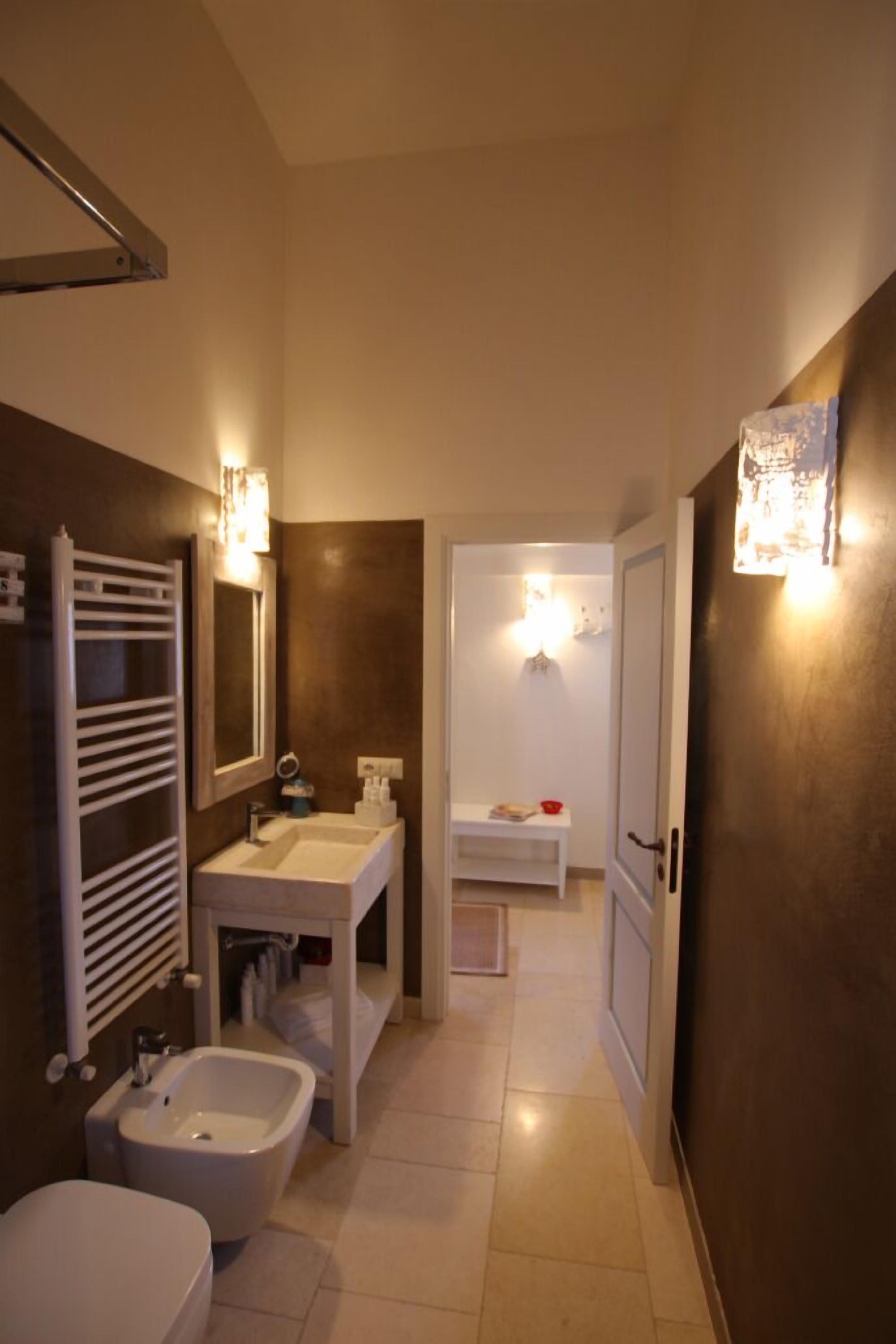 Ein modernes Badezimmer mit Waschbecken, Bidet und Toilette in Weiß. Zwei Wandleuchten und ein Handtuchhalter sind vorhanden.