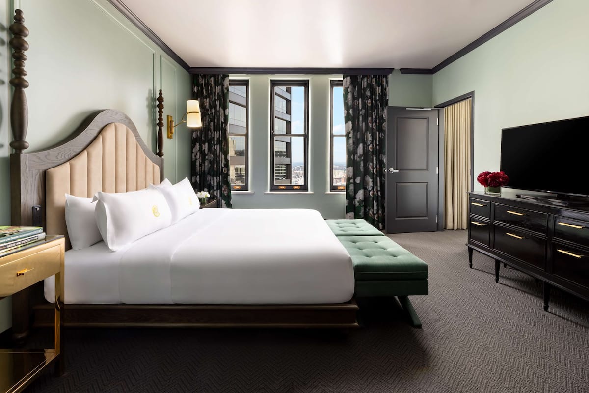 A hotel room with a large bed, a television, a dresser, and a window with curtains.