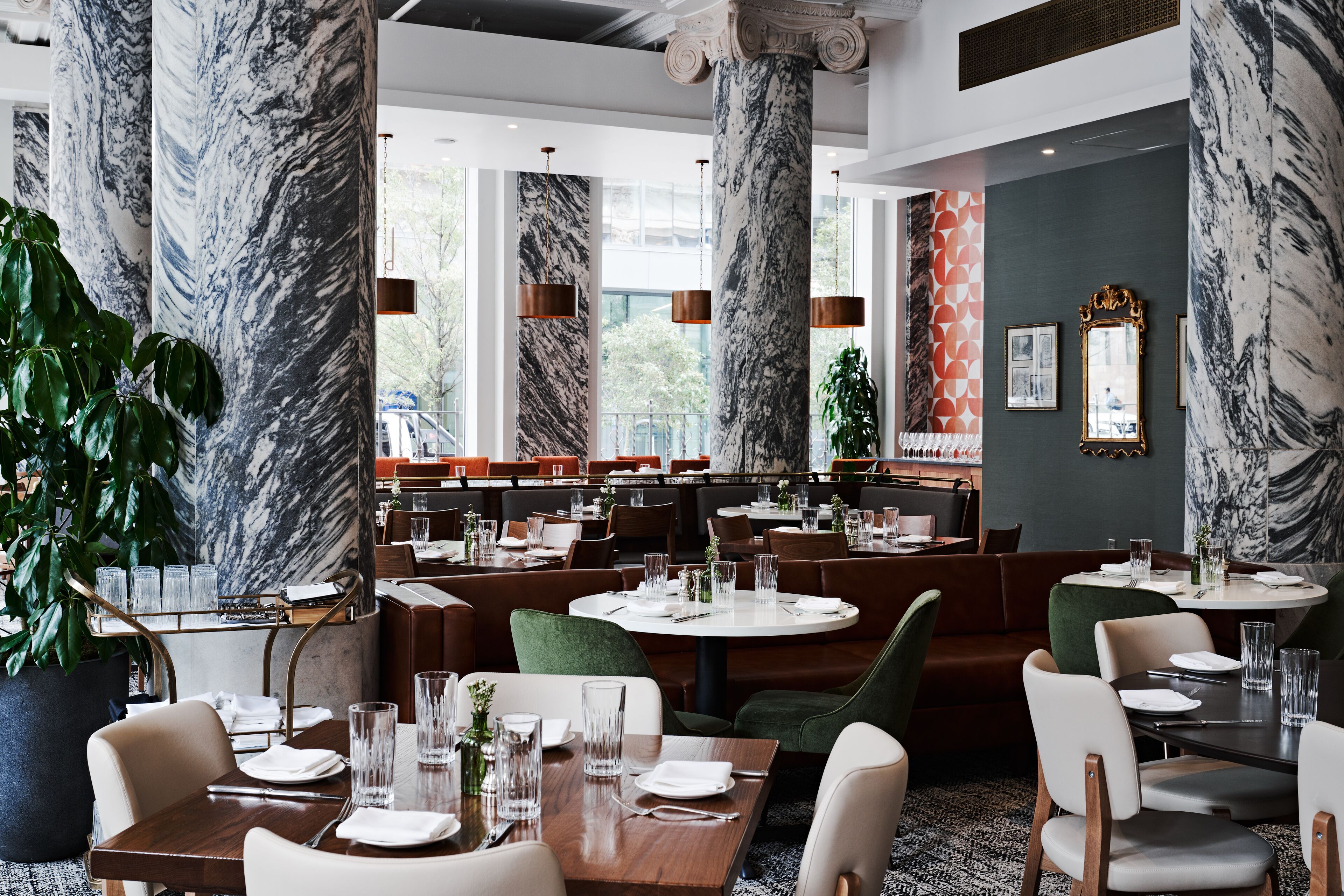 A restaurant with marble columns, green upholstered booths, and neatly set tables with glassware and plates.