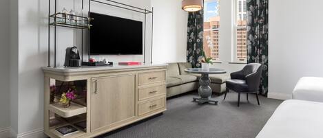 Una habitación de hotel con televisor de pantalla plana, un mueble de madera con cajones, una mesa redonda con una silla, un sofá y una cama.