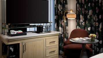 Een hotelkamer met een flatscreen-televisie, een koffiezetapparaat, een tafeltje met een lamp, een stoel en een vaas met bloemen.