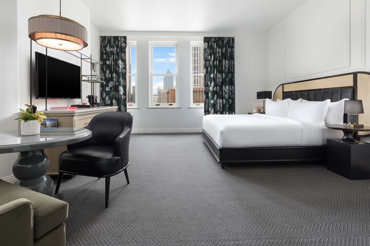 A hotel room with a bed, a desk, a chair, a TV, and a view of the city.