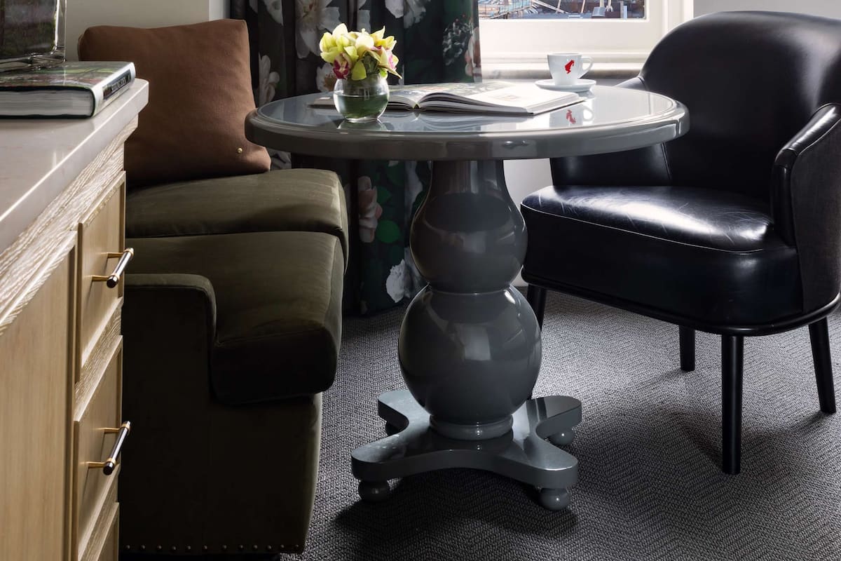 A room with a view of a Ferris wheel, a round table with a lamp, a sofa, a chair, and a cabinet.