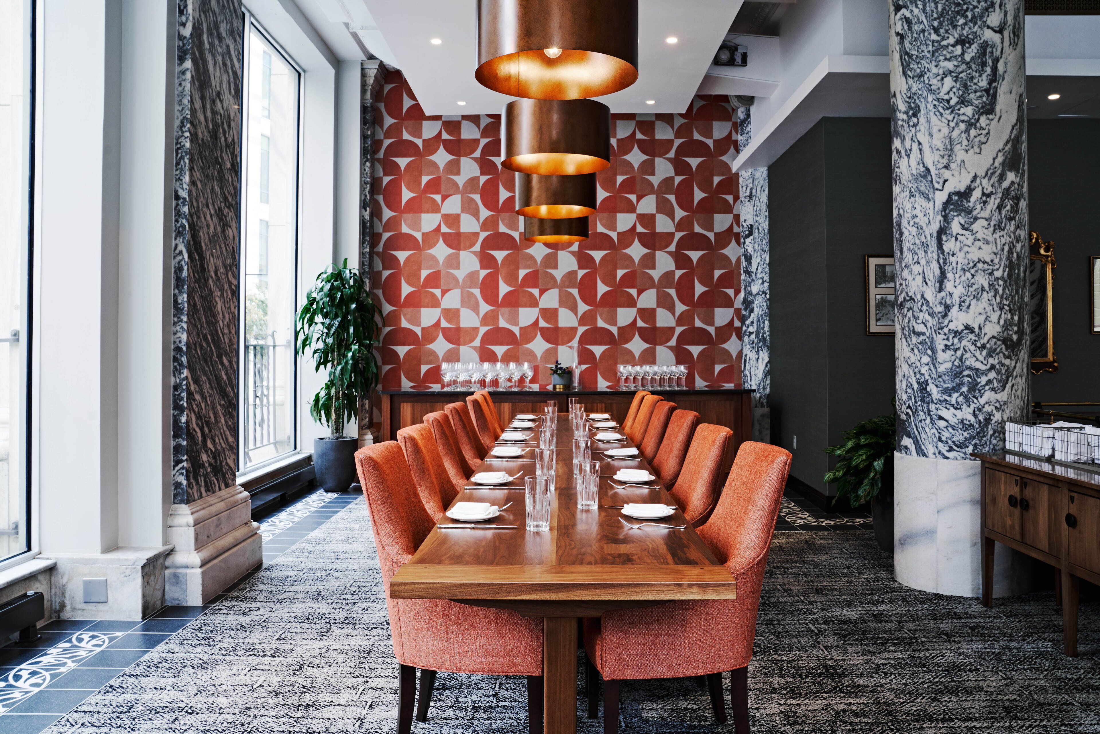 A conference room with a long table, orange chairs, and a patterned wall.