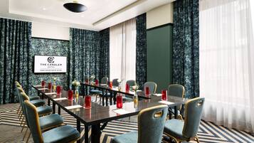 A conference room with a long table, chairs, and a screen displaying the hotel name.