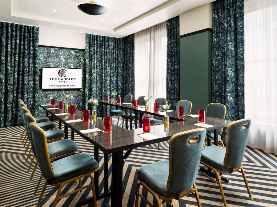 A conference room with a long table, chairs, and a screen displaying the hotel name.