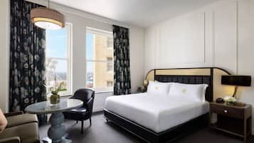 A hotel room with a large bed, a round table, a chair, and a nightstand with a lamp.