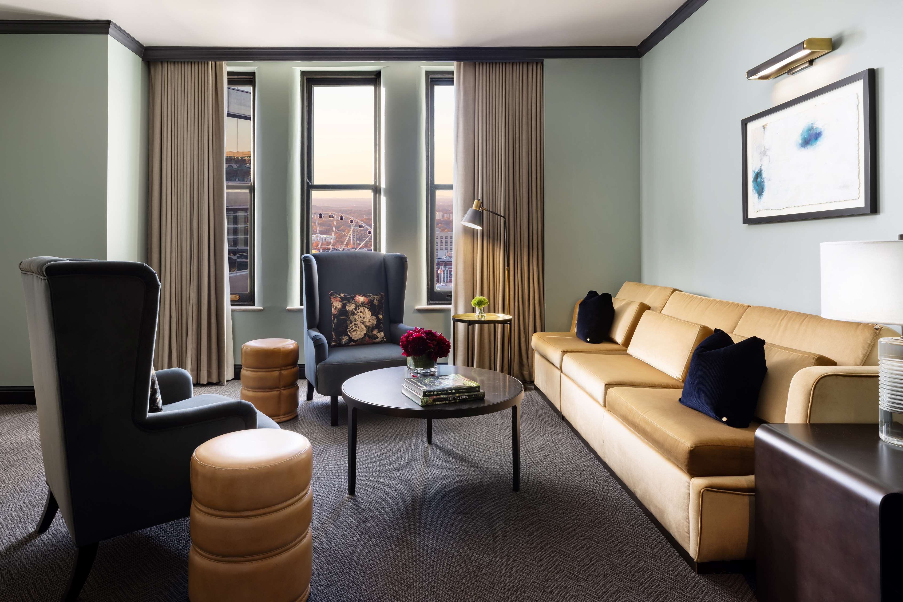 Une chambre d’hôtel moderne avec un canapé, un fauteuil, un pouf et une table basse agrémentée de livres et de fleurs.