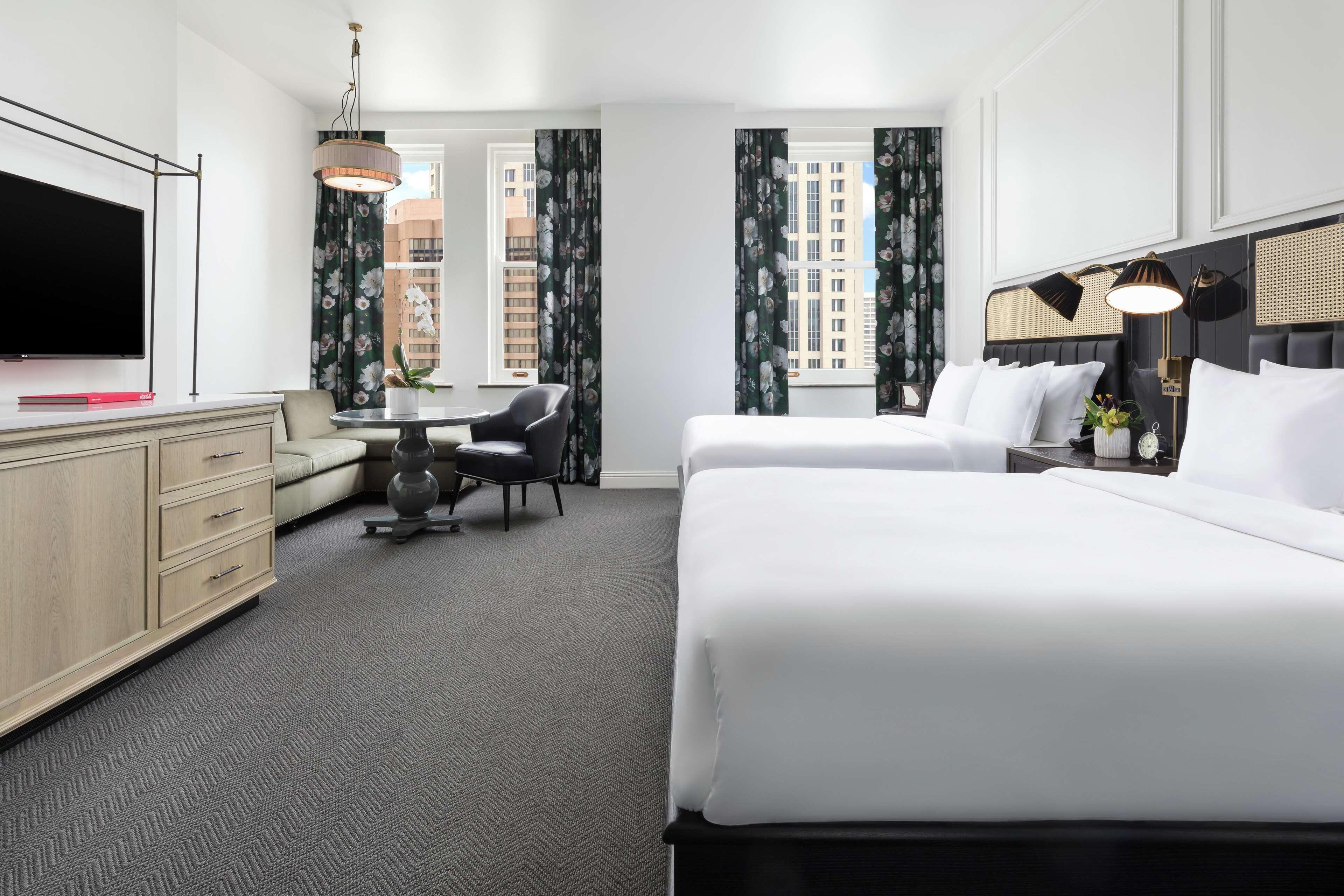 A hotel room with a large bed, a desk, a chair, a TV, and a window with curtains.