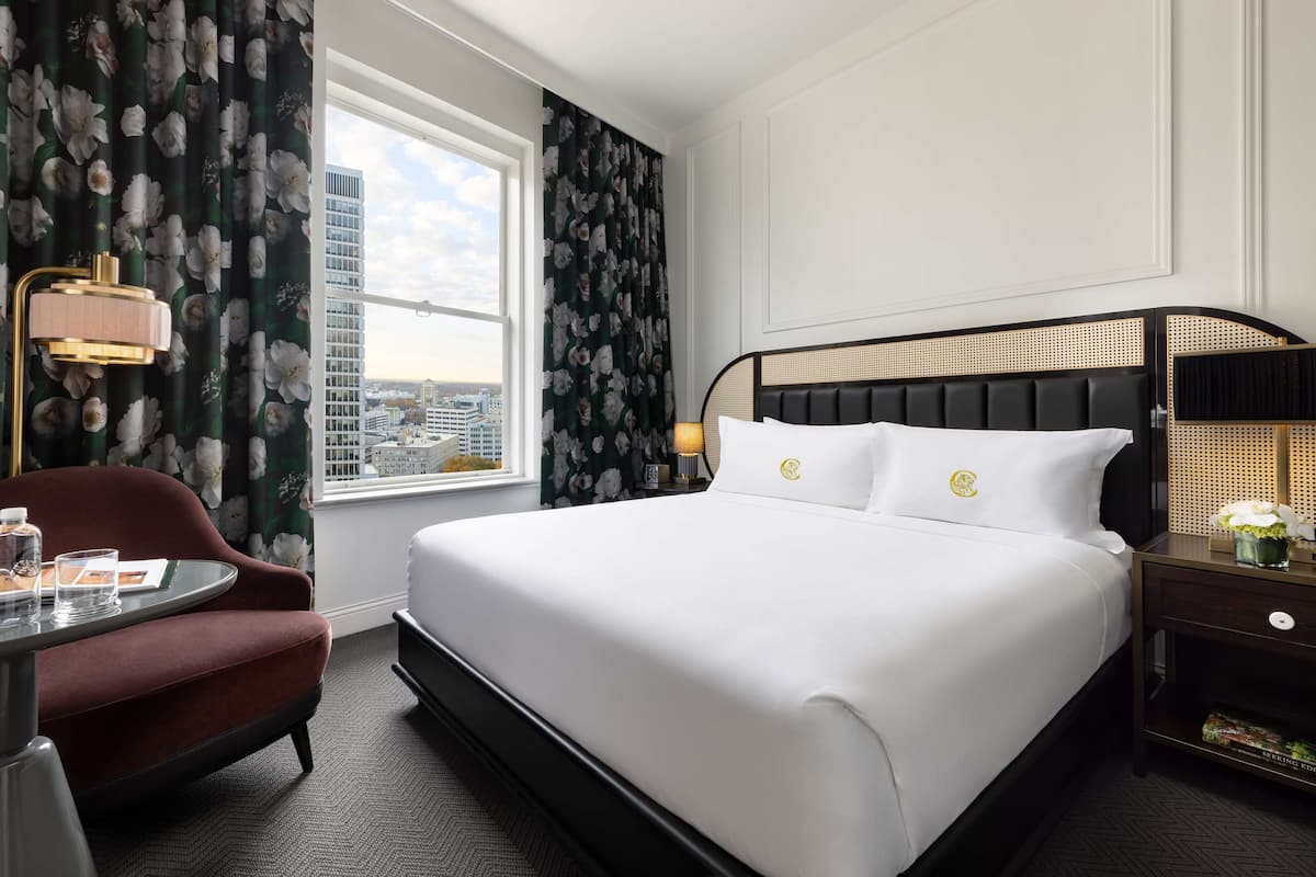 A hotel room with a large bed, a desk, a chair, and a window with curtains.