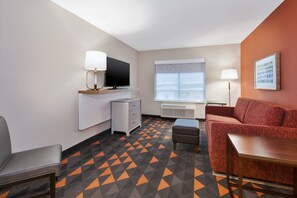 Et hotelværelse med fjernsyn, sofa, lille bord, stol og et mønstret tæppe.