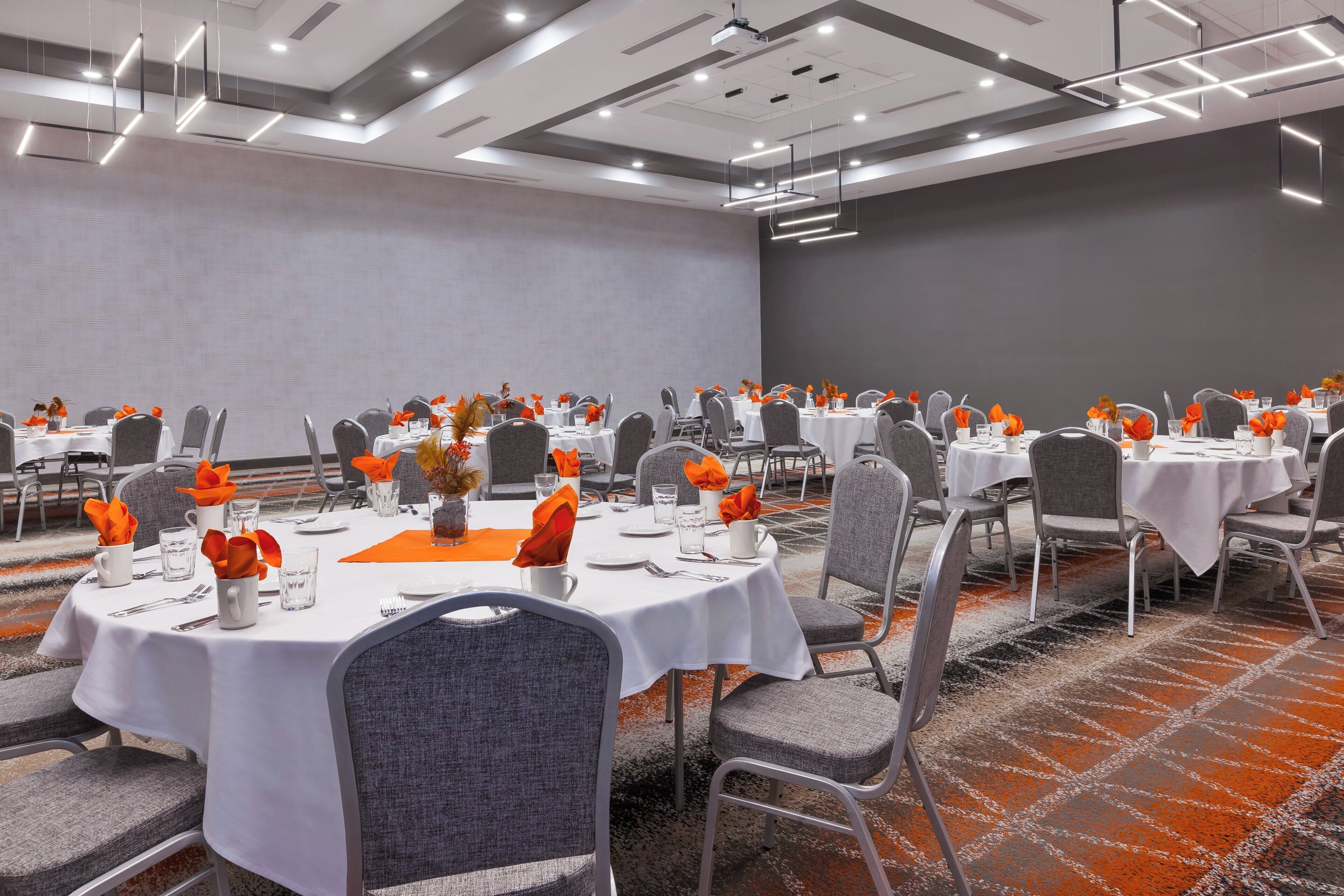 Una sala de conferències amb diverses taules preparades per dinar, equipada amb cadires i coberts.