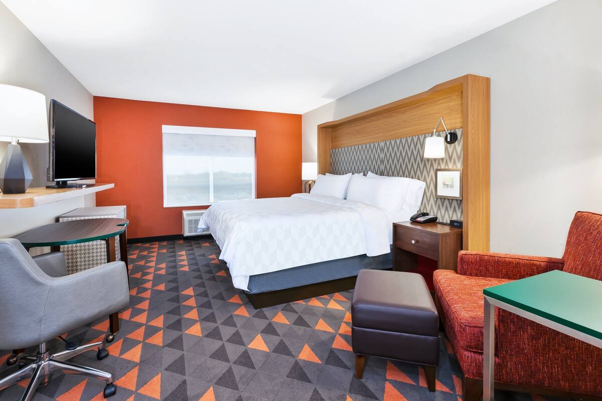 Ein Hotelzimmer mit Bett, Schreibtisch mit Computer, Stuhl und Fernseher.