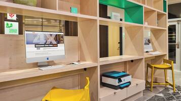 A hotel reception desk with a computer monitor, keyboard, and mouse. There are two yellow chairs and a green vase on the shelf.