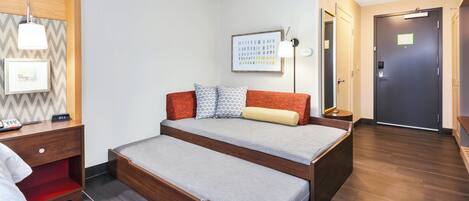 Una habitación con cama, mesita de noche, lámpara, un cuadro enmarco y una puerta.