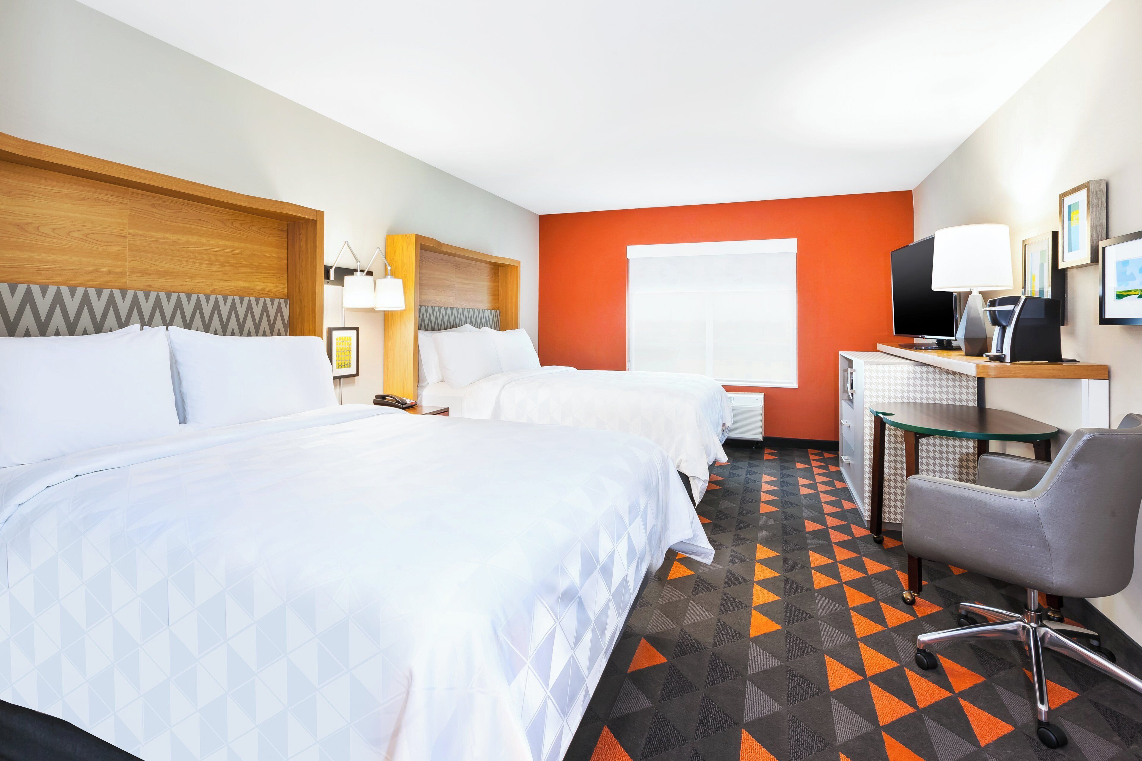 A hotel room with two beds, a desk with a computer, a chair, and a television.