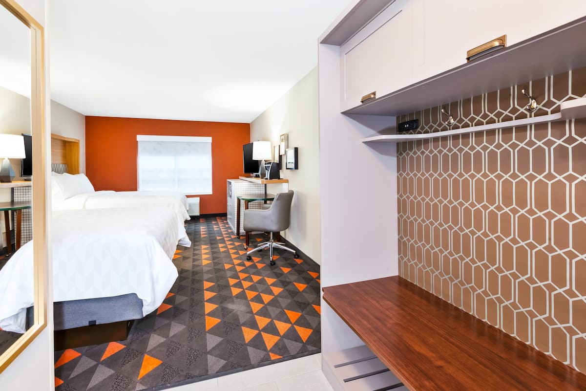 Ein Hotelzimmer mit zwei Betten, einem Schreibtisch mit Computer, einem Stuhl und einer Wand mit Muster.