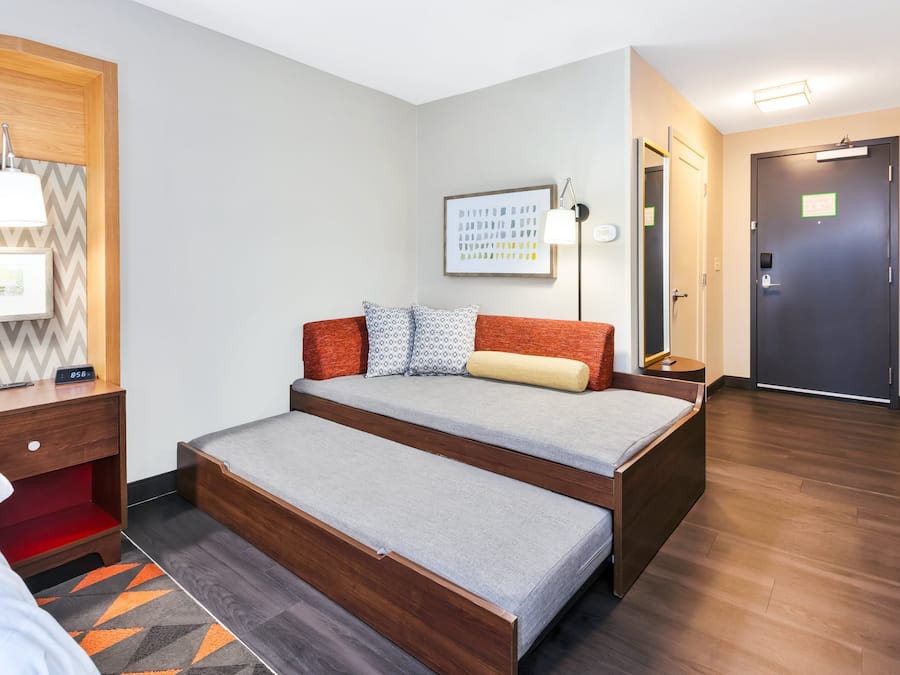 A room with a bed, bedside table, lamp, framed picture, and a door.