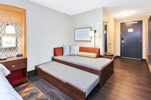 A room with a bed, bedside table, lamp, framed picture, and a door.