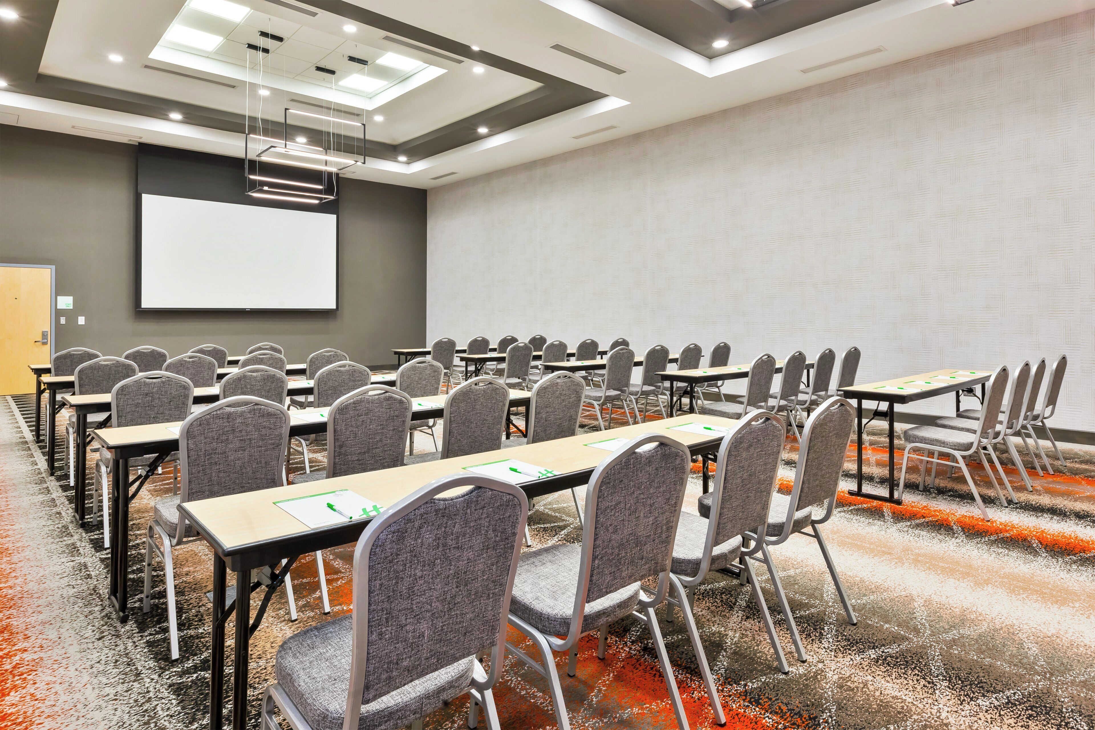 A conference room with rows of tables and chairs, a projector screen, and a whiteboard.