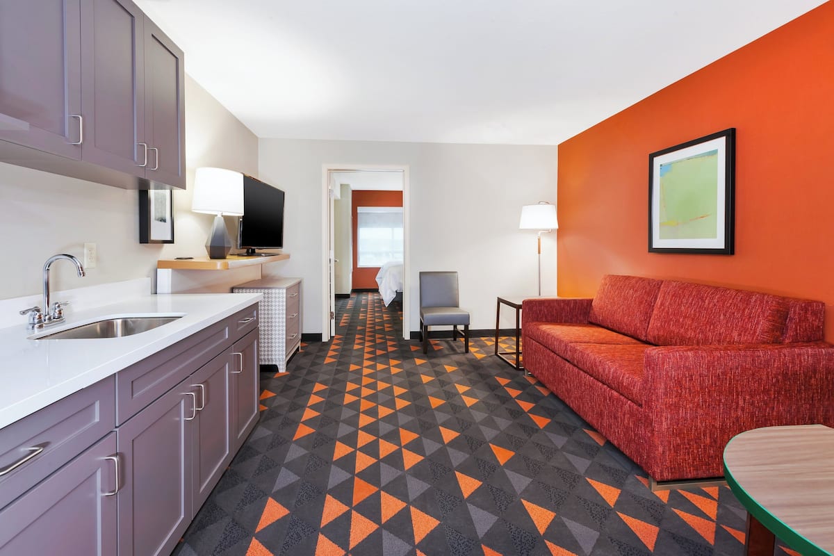 Ein Hotelzimmer mit Küchenzeile, einem roten Sofa, einem kleinen Tisch und einem gestreiften Boden.