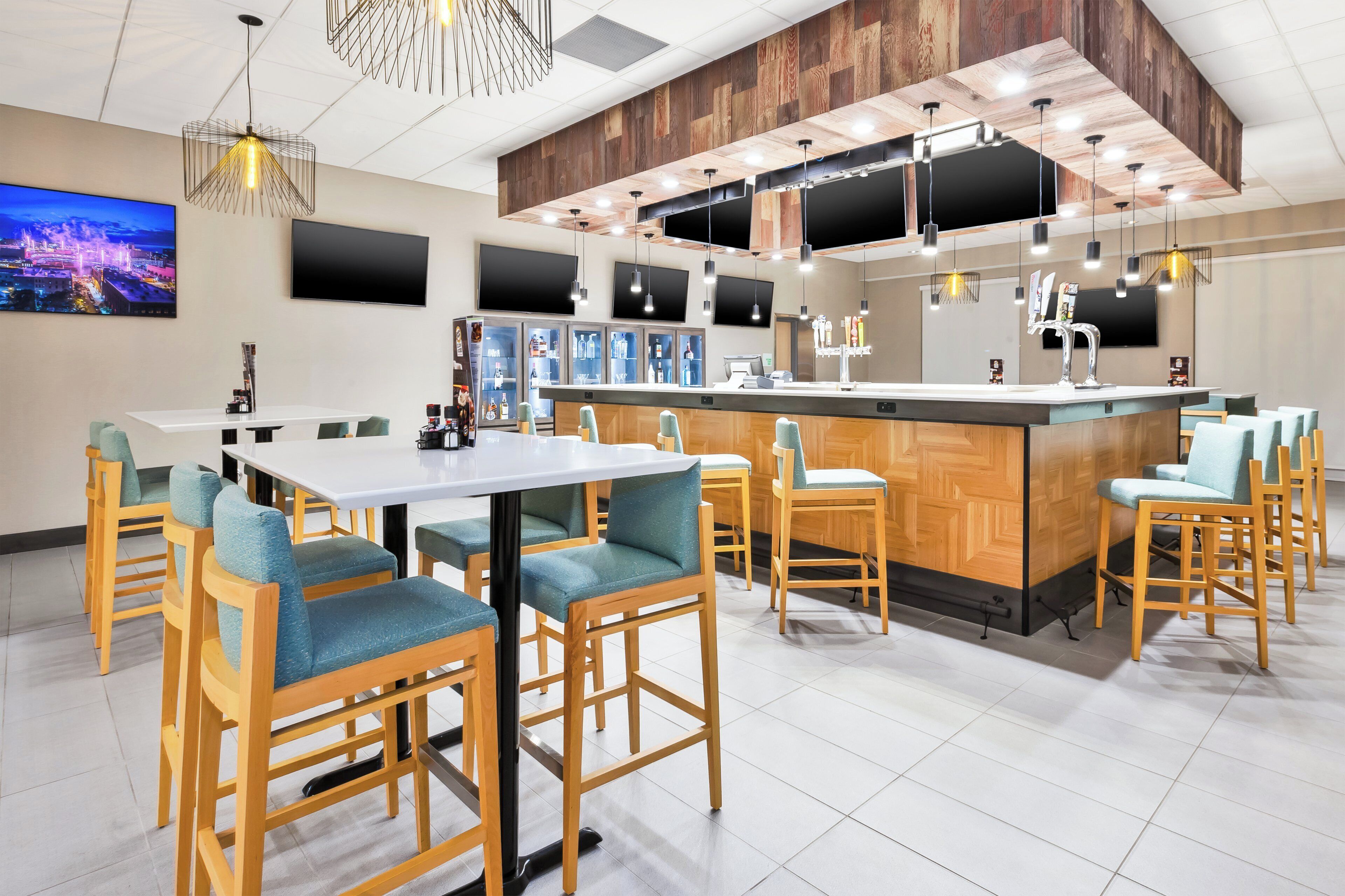 A modern bar area with wooden furniture and a bar counter, equipped with multiple screens and a selection of beverages.