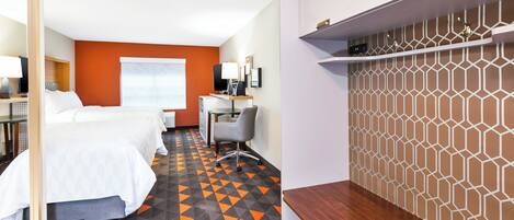 Une chambre d’hôtel avec deux lits, un bureau avec un ordinateur, une chaise et un mur décoré de motifs.