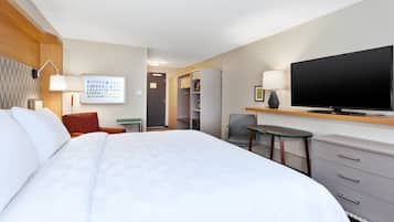 Habitación de hotel con una cama grande, un televisor de pantalla plana, un escritorio con una silla, una mesita pequeña y un armario.