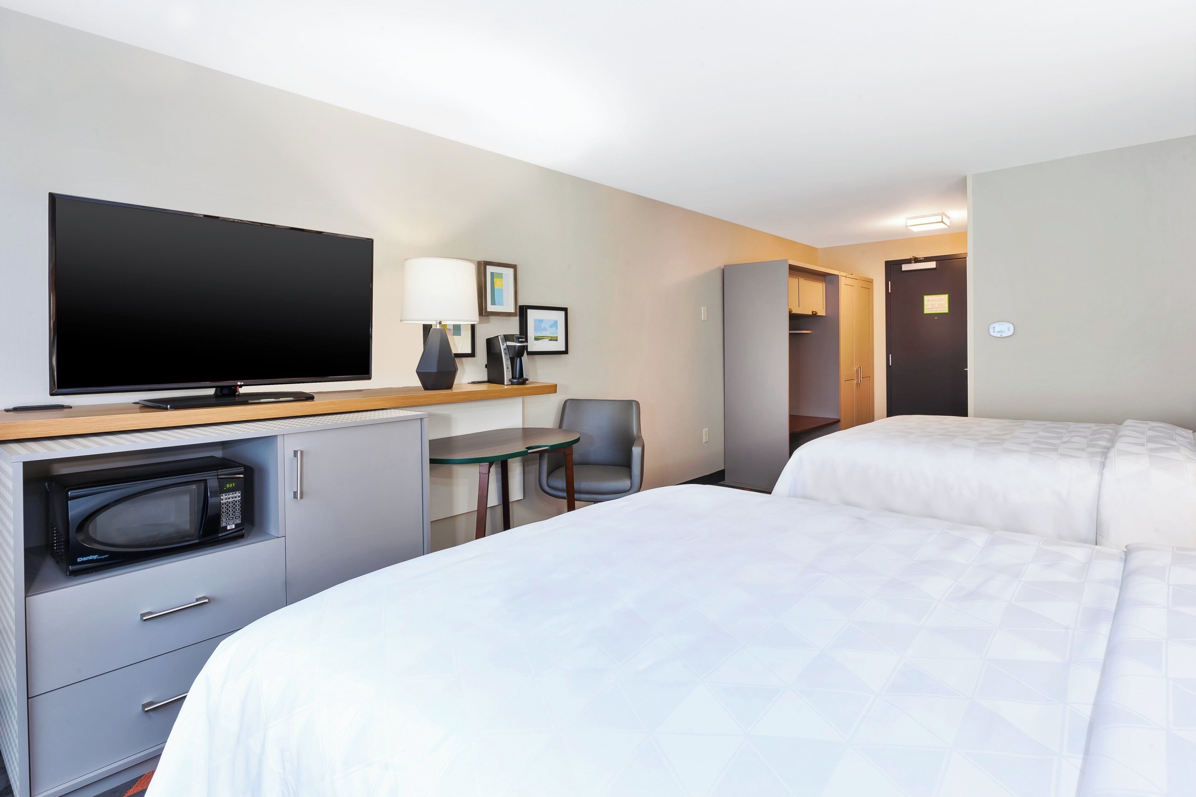 A hotel room with a bed, a desk with a television, a microwave, a chair, and a wardrobe.