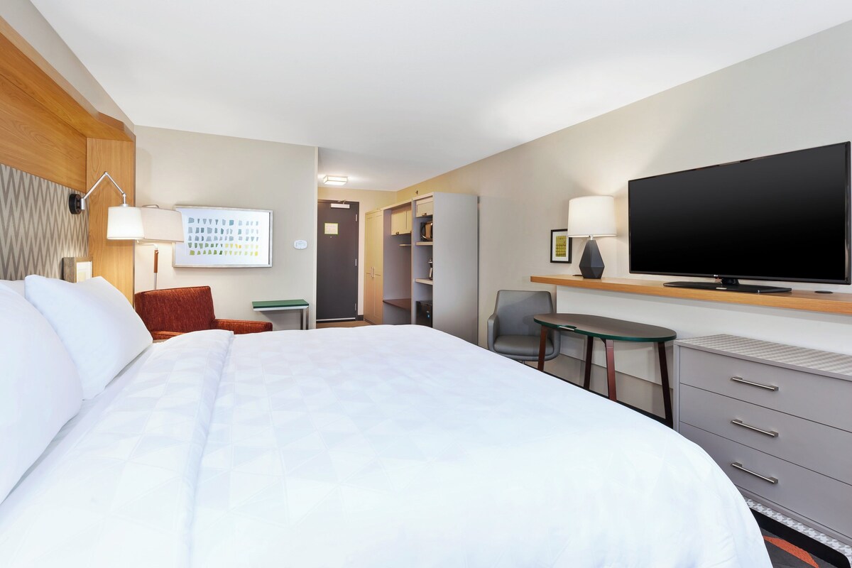 Et hotelværelse med en stor seng, et fladskærms-TV, et skrivebord med stol, et lille bord og et garderobeskab.