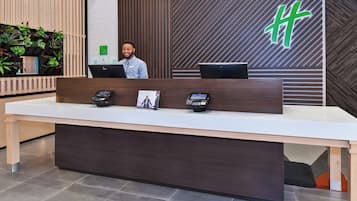 Un mostrador de recepción con un quiosco de registro digital, una laptop y un cartel con un logotipo verde.