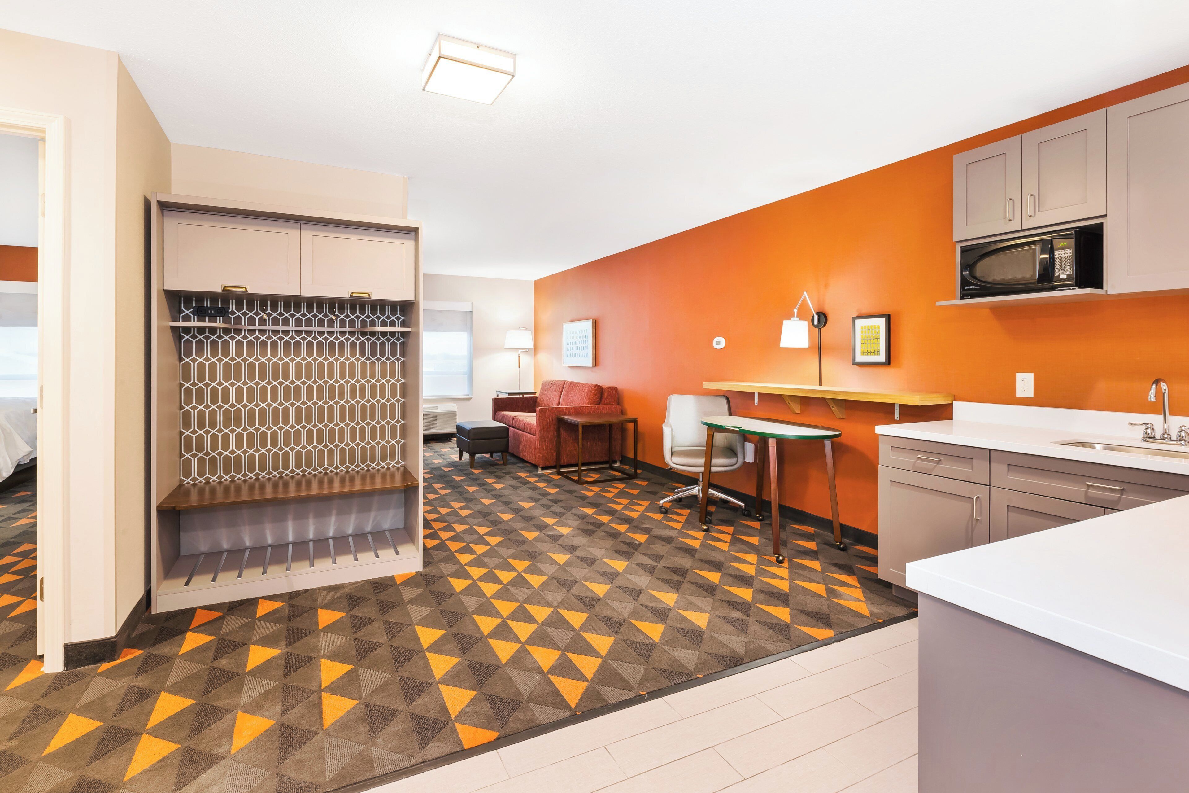 Habitación de hotel con kitchenette, zona de estar con sofá y sillones, y piso estampado.