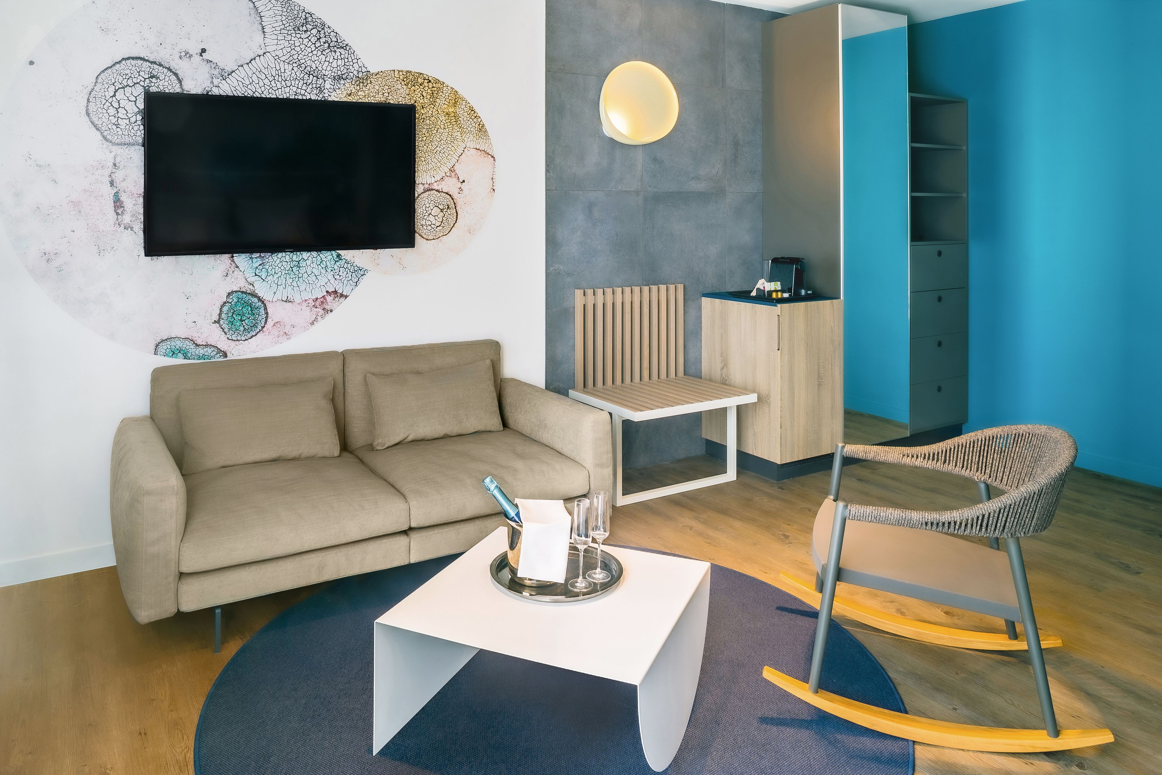 A modern living room with a sofa, a coffee table with a bottle and glasses, a TV mounted on the wall, and a wooden cabinet.