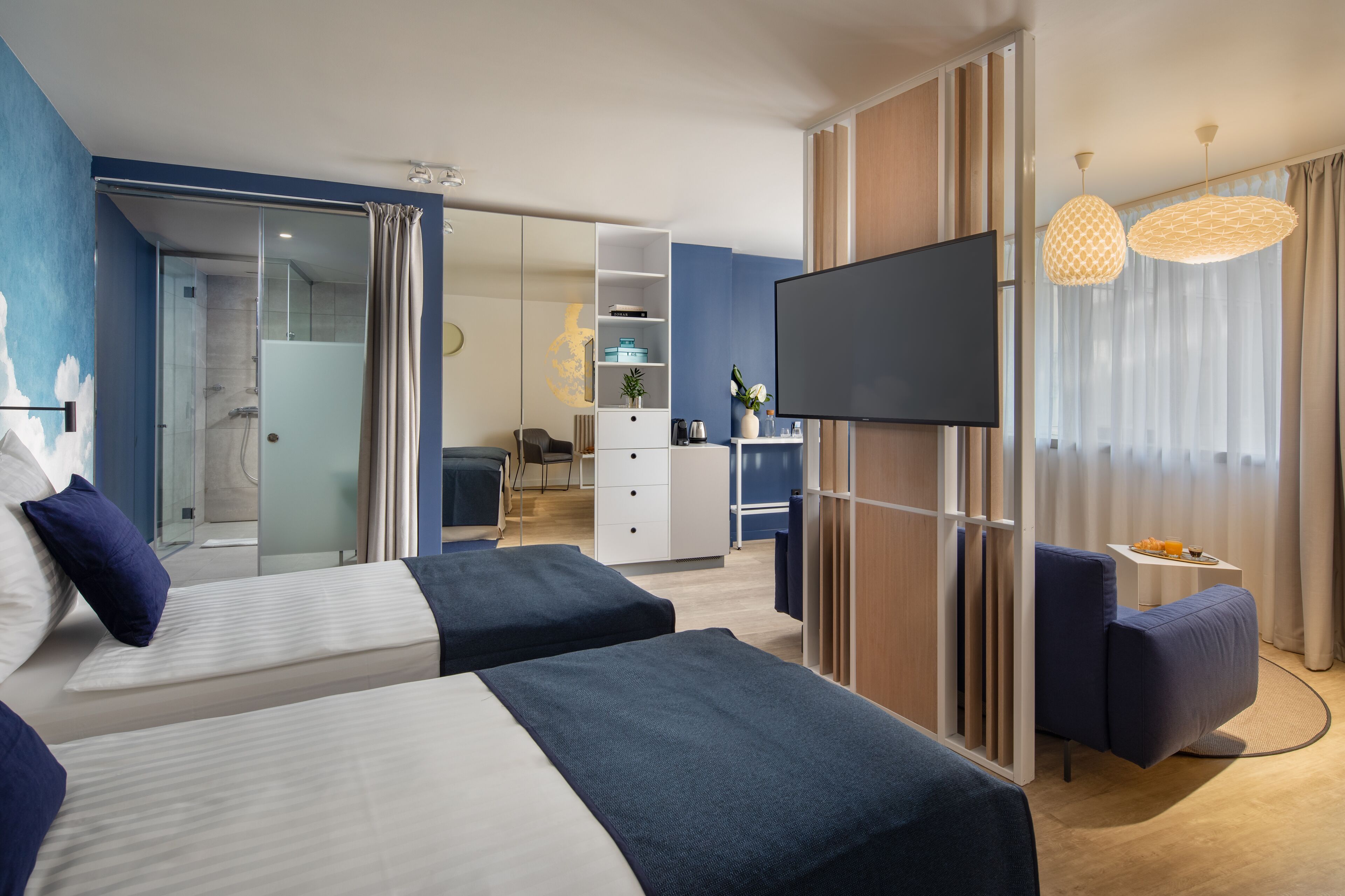 Una habitación de hotel moderna con dos camas, televisión, escritorio y zona de ducha.