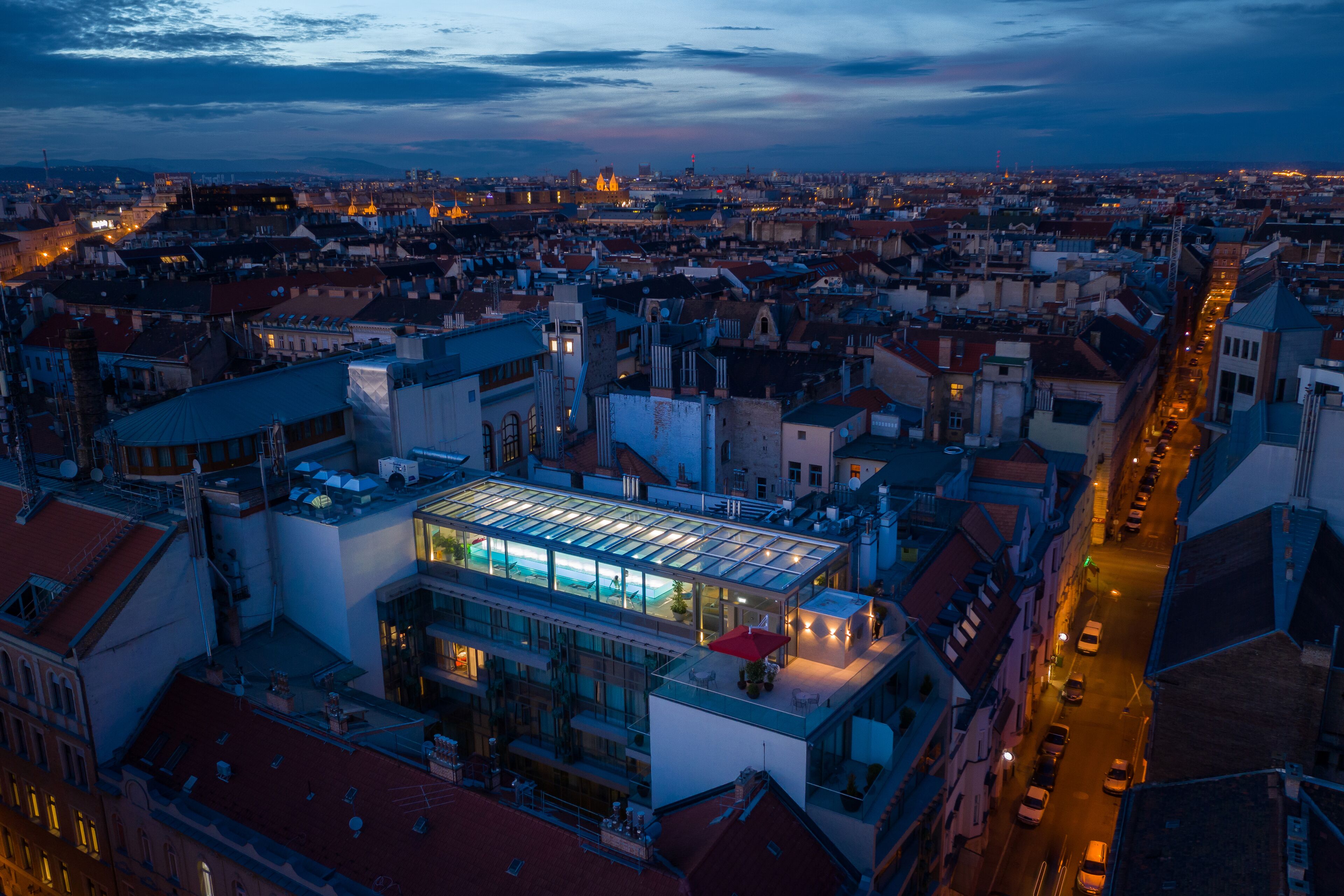 A modern hotel with a glass atrium, located in a densely built urban area with surrounding buildings and a busy street.