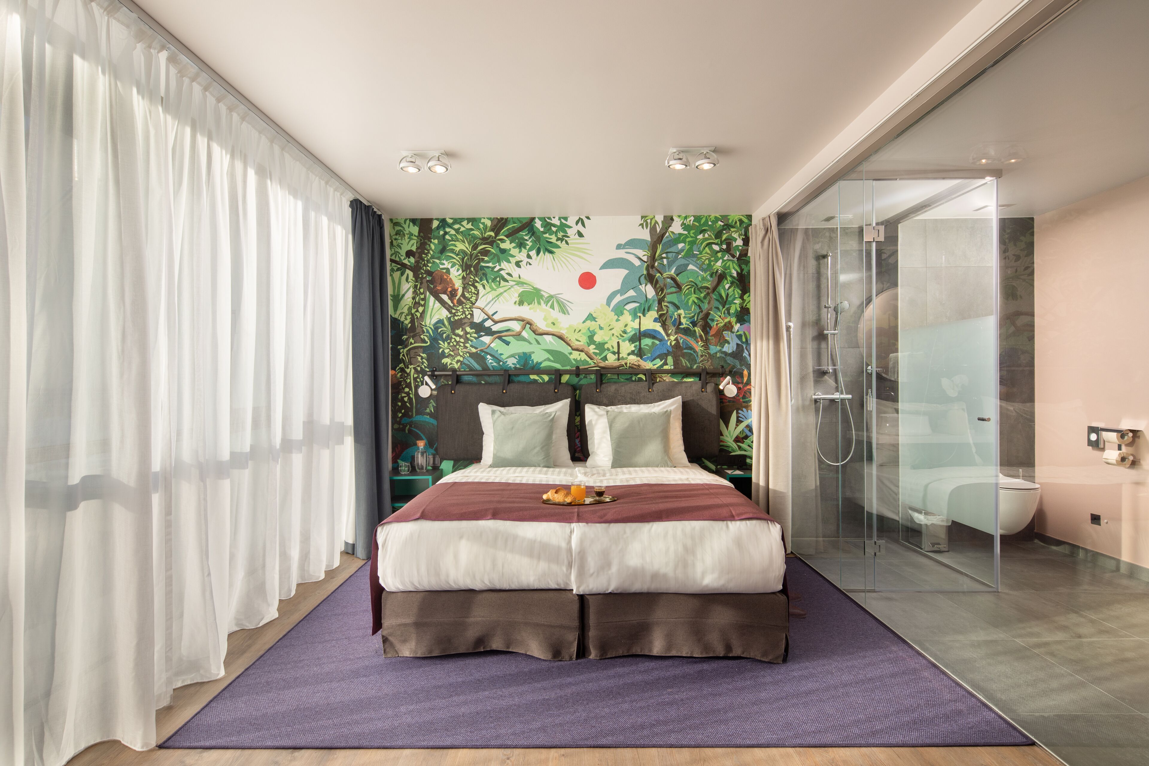 Een moderne hotelkamer met een groot bed, een douchecabine van glas en een muurschildering.