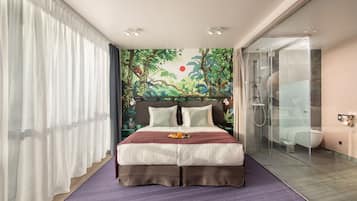 Een moderne hotelkamer met een groot bed, een douchecabine van glas en een muurschildering.