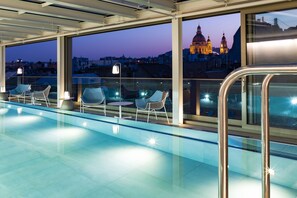 A rooftop pool area with seating and a view of a historic building at dusk. - Cortile Hotel - Adult only (Budapest)