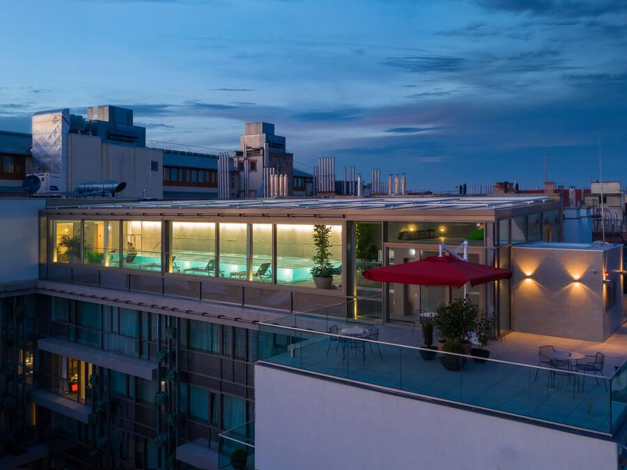 A rooftop pool area with glass walls, a hot tub, and outdoor seating.