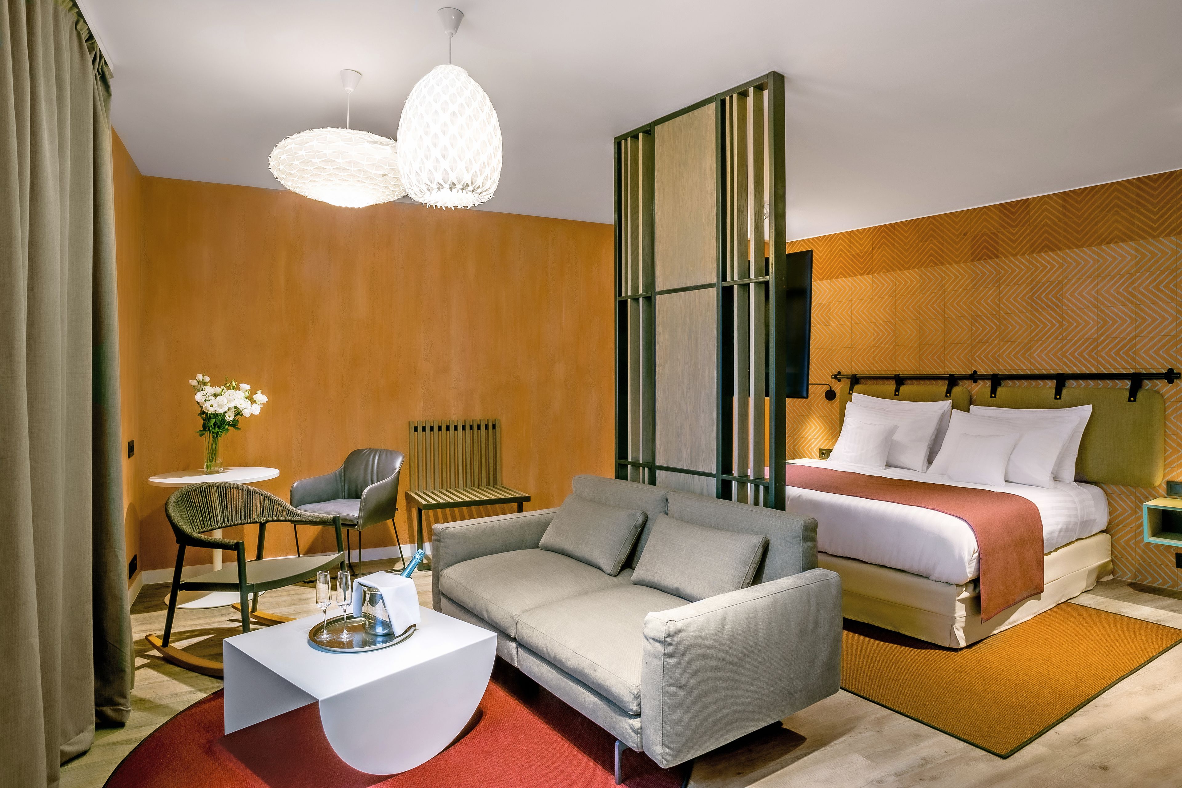 Quarto de hotel moderno com sofá, cama, mesa de centro e abajur decorativo.