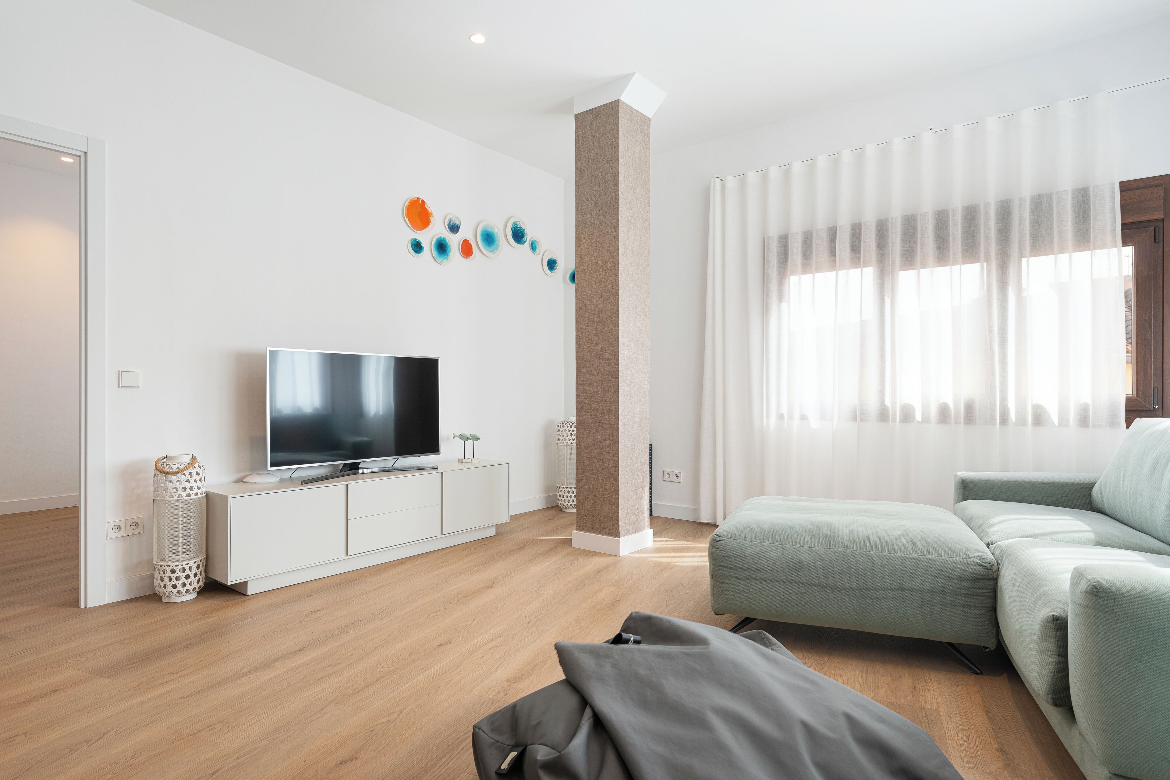 Una sala de estar moderna con un televisor de pantalla plana, un sofá de color claro y piso de madera.