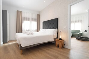 Een moderne slaapkamer met een groot bed, houten vloeren en een klein nachtkastje met een lamp.