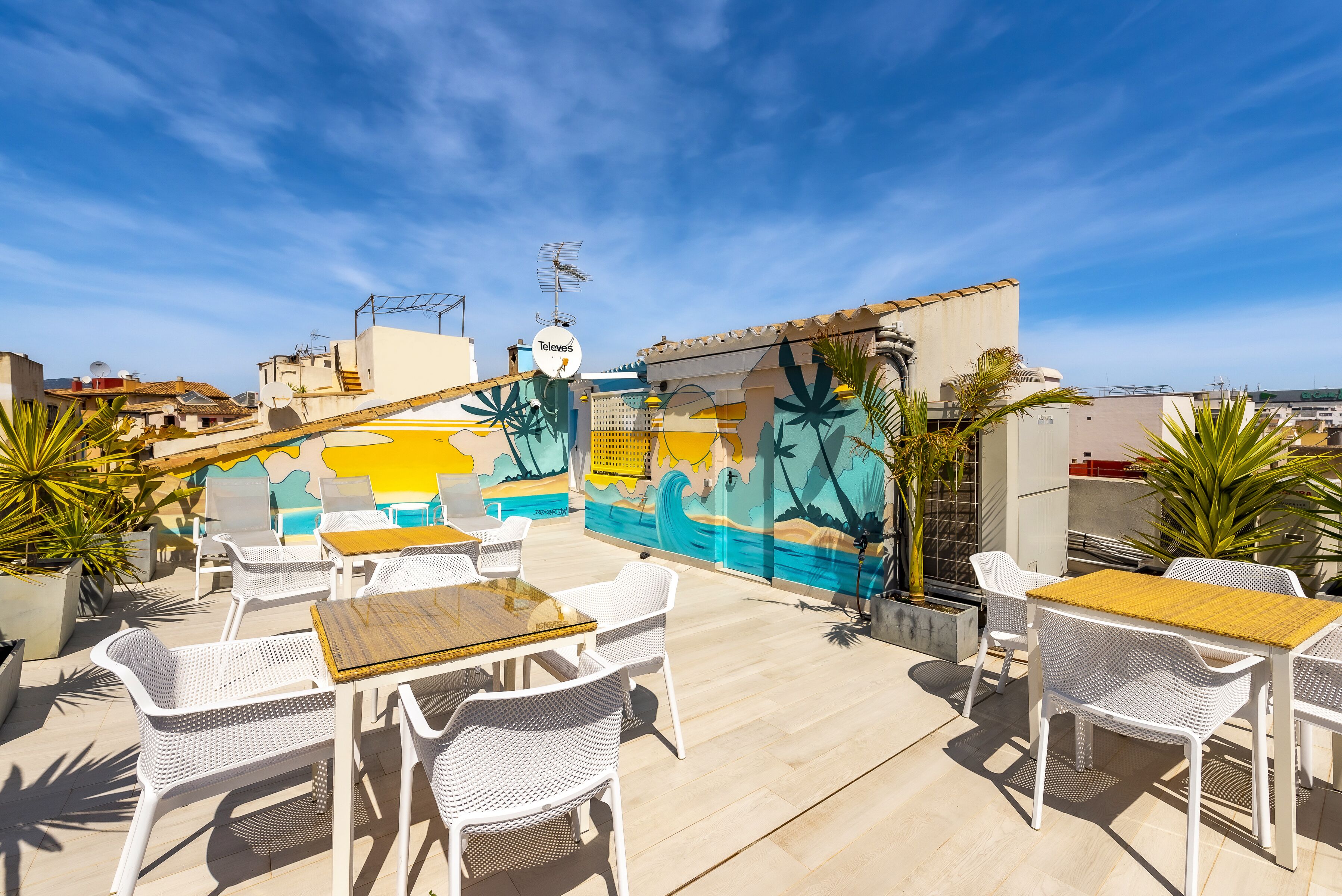 Une terrasse extérieure avec des meubles en osier blanc et une fresque murale.
